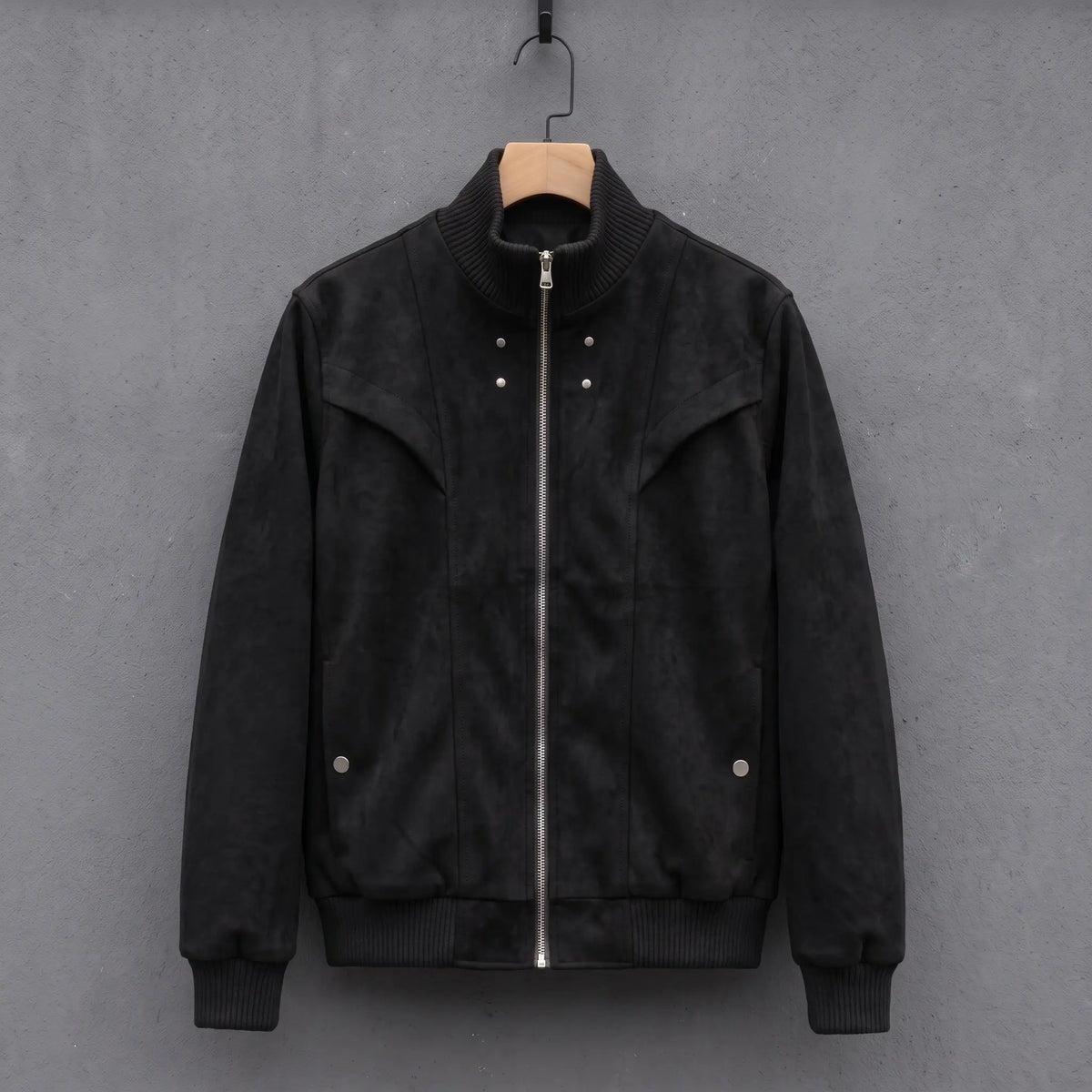 Black suede bomber jacket with ribbed stand collar on a wooden hanger, front view