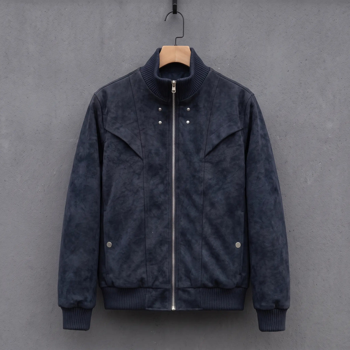 Dark blue suede bomber jacket with ribbed stand collar on a wooden hanger, front view