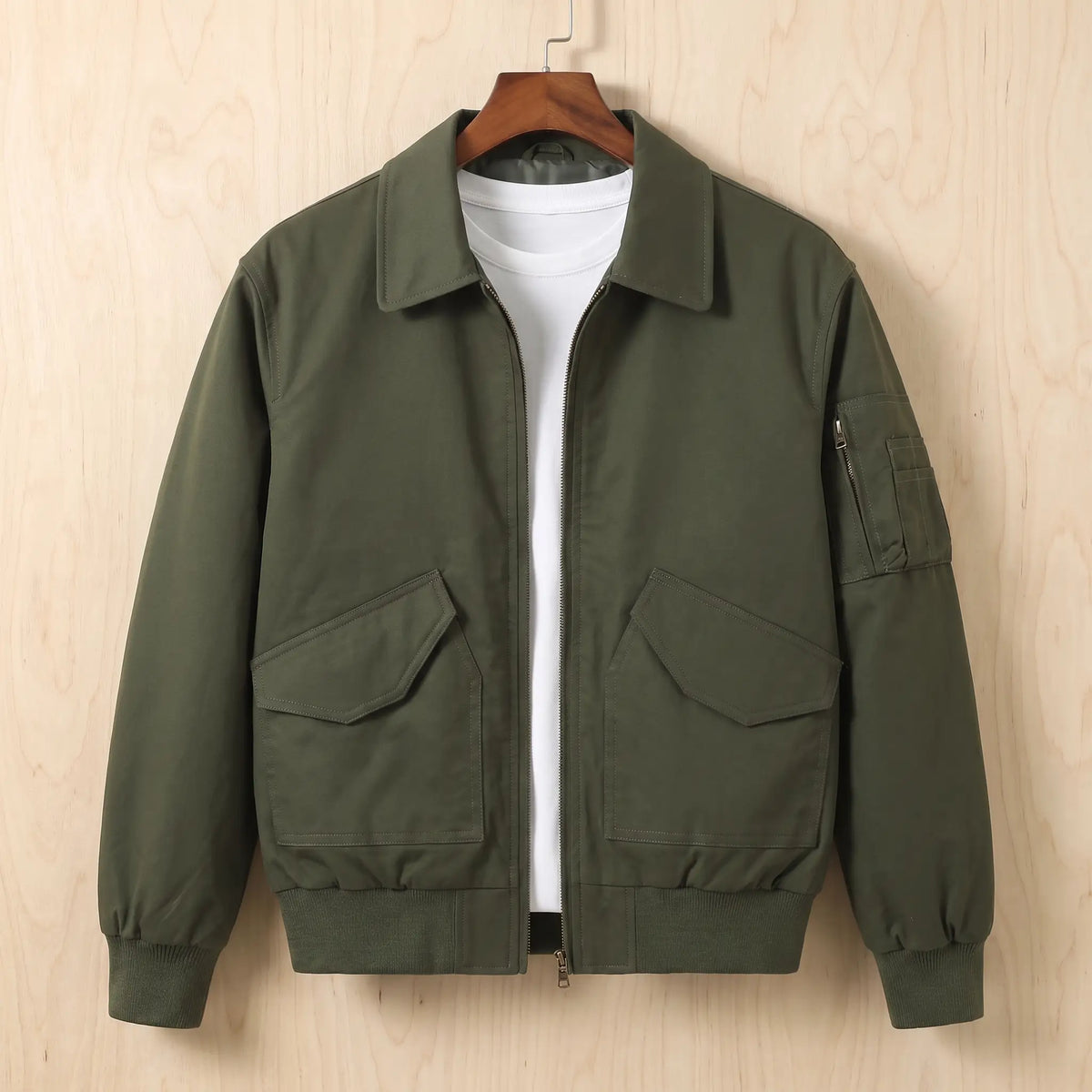 Sleeve Pocket Bomber in green, a short flight bomber jacket with a zip front, hip flap pockets and a zipped sleeve pocket on a wooden hanger