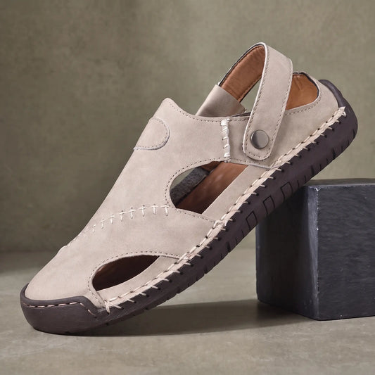 Snap Strap Sandals in beige, a closed toe leather fisherman sandal with cut out side panels and a metal snap instep strap, on a charcoal slate block