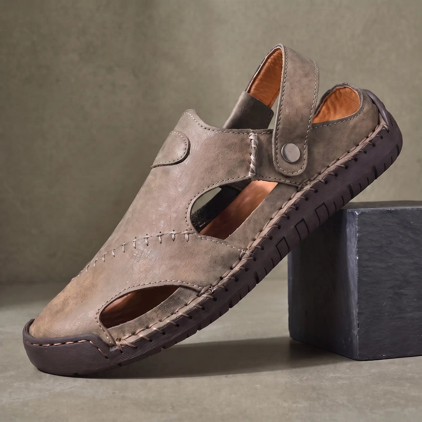 Snap Strap Sandals in grey, a closed toe leather fisherman sandal with cut out side panels and a metal snap instep strap, on a charcoal slate block