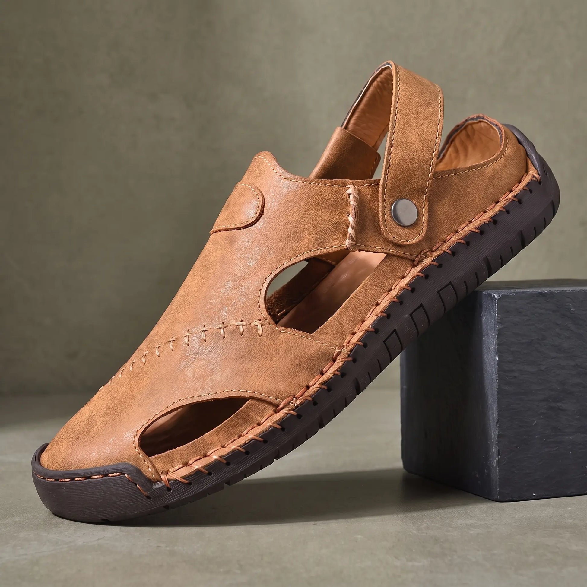 Snap Strap Sandals in light brown, a closed toe leather fisherman sandal with cut out side panels and a metal snap instep strap, on a charcoal slate block