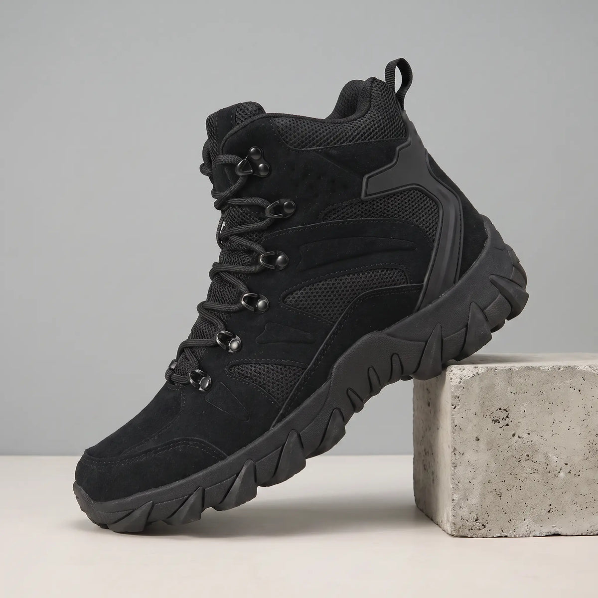 Soft Suede Hikers in black, a mid cut suede and mesh boot with fabric lace loops and a toothed sole, on a concrete block