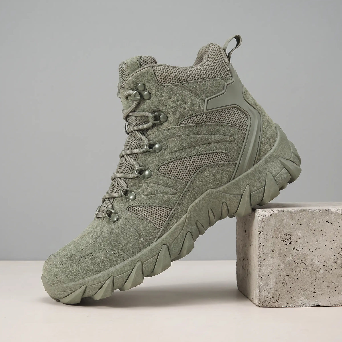 Soft Suede Hikers in green, a mid cut suede and mesh boot with fabric lace loops and a toothed sole, on a concrete block