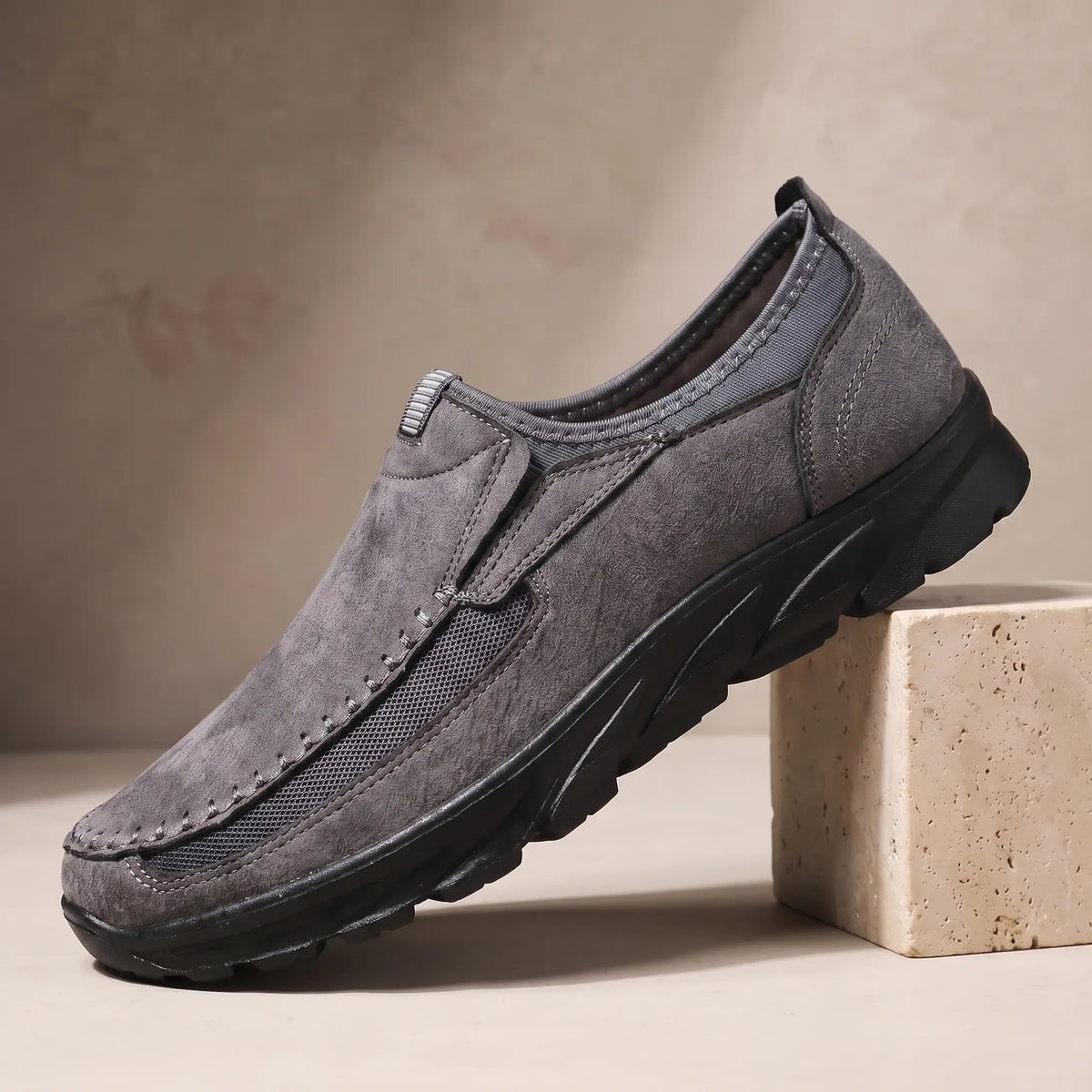 Stitched Apron Loafers in grey, a slip on moccasin loafer with elastic side panels and a chunky black bottom, on a travertine display block