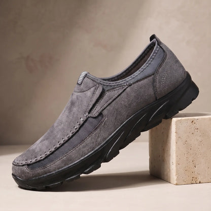 Stitched Apron Loafers in grey, a slip on moccasin loafer with elastic side panels and a chunky black bottom, on a travertine display block