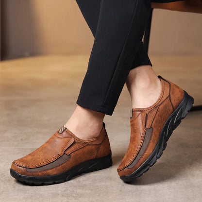 Man seated with ankles crossed wearing the light brown Stitched Apron Loafers with dark trousers