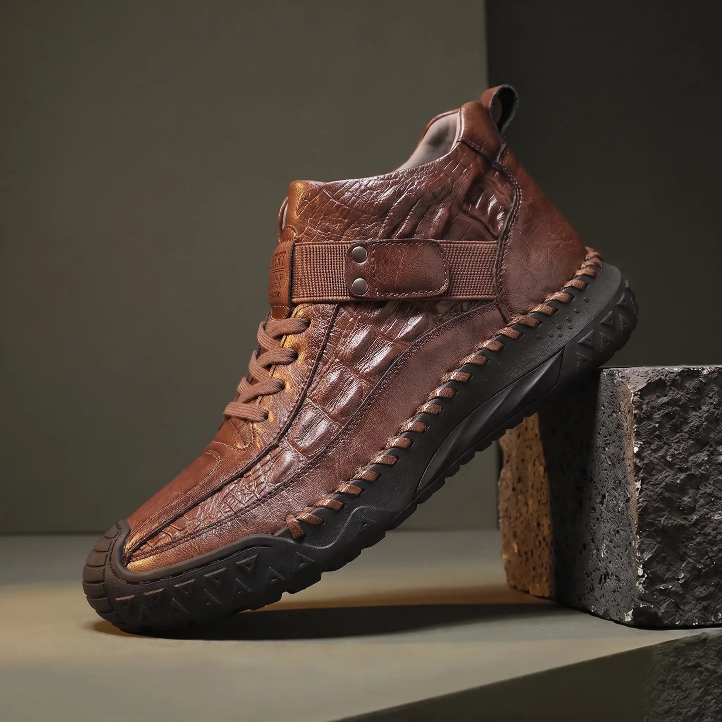 Dark brown high top boot with croc embossed panel on a basalt block